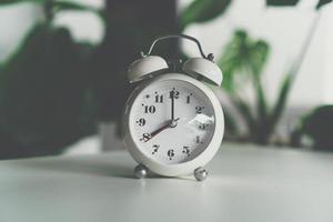 Selective focus of alarm clock showing 8 o'clock on table with nature bokeh background photo