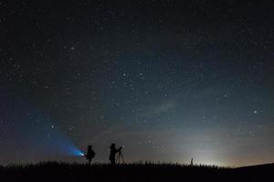 Fotógrafos de silueta con un cielo lleno de estrellas de fondo en la noche foto