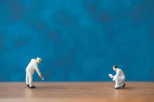 Miniature people holding a brush in front of a blue wall background photo