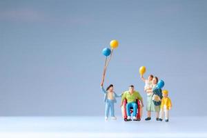 Las personas en miniatura muestran una familia positiva cuidando a su padre discapacitado. foto