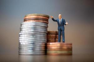 Pequeños empresarios en miniatura de pie con una pila de monedas, concepto de crecimiento empresarial foto