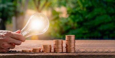 A person holding a light bulb over stacks of coins photo