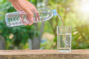 Botella de agua potable y vaso con fondo natural. foto