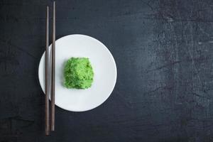 Wasabi en un plato blanco con un par de palillos sobre fondo negro de la tabla foto