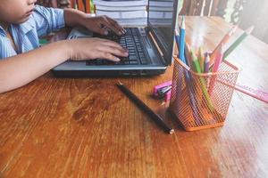 Boy working on a laptop next to cup of pencils on a wooden desk photo