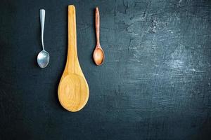 Two wooden spoons and a metal spoon on a black table background