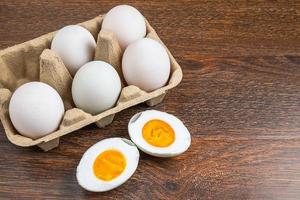 Sliced hard-boiled duck egg next to whole eggs in a carton on a wooden table photo