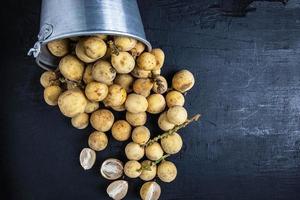 Longkong or langsat fruit spilling out of a metal bucket on a black wood background photo