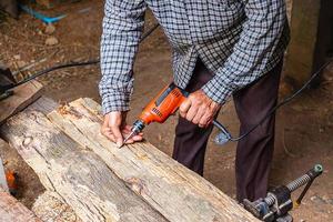 Hombre con taladro eléctrico en la plancha de madera en un taller de carpintería foto