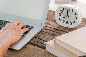 A person typing on a laptop computer next to a clock photo