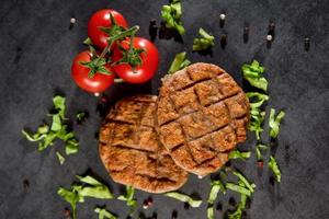 Burger patties on slate stone black board with tomato photo