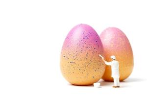 Miniature person painting Easter-eggs for Easter day on a white background