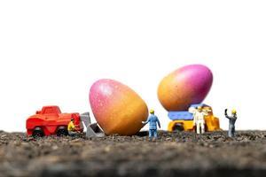 Miniature people working on Easter Eggs for Easter day with a white background photo