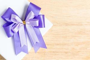 Purple ribbon bow on a white gift box on a wooden background photo