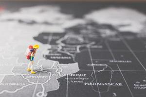 Mochilero en miniatura caminando sobre un mapa del mundo, el turismo y el concepto de viaje foto