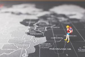 Mochilero en miniatura caminando sobre un mapa del mundo, el turismo y el concepto de viaje