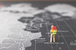 Mochilero en miniatura caminando sobre un mapa del mundo, el turismo y el concepto de viaje