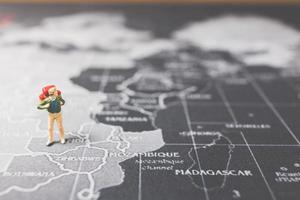 Mochilero en miniatura caminando sobre un mapa del mundo, el turismo y el concepto de viaje foto