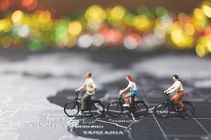 Miniature travelers riding a bicycle on a world map, traveling and exploring the world concept photo