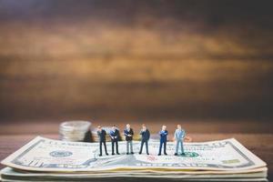 Miniature businessmen on money on a wooden background