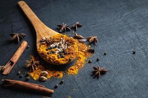 Colorful spices and powder on a wooden spoon on a black table background photo