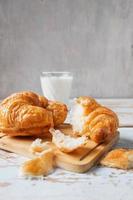 Croissants sobre una tabla para cortar madera junto al vaso de leche en la mesa de madera azul foto