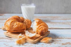 Croissants on a wood cutting board next to glass of milk on blue wooden table photo