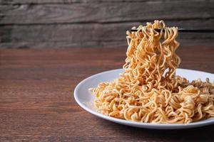 Pair of chopsticks picking up instant noodles on a white plate on a wooden table photo