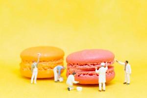 Miniature painters coloring macaroons on a yellow background photo