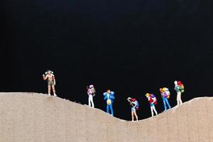 Miniature travelers with backpacks walking on a paper mountain, travel and trekking concept photo