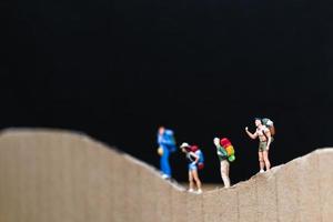 Miniature travelers with backpacks walking on a paper mountain, travel and trekking concept photo