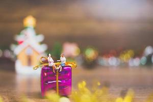Miniature people on a gift box with Christmas celebration decoration in the background photo