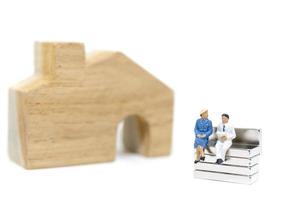 Miniature husband and wife sitting in front of a house on a white background, family concept photo