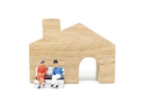 Miniature husband and wife sitting in front of a house on a white background, family concept photo