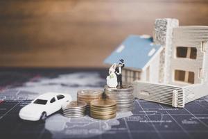 Miniature bride and groom with coins in front of a home, successful family concept photo