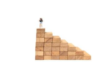 Miniature backpacker standing on wood blocks isolated on a white background, travel concept photo