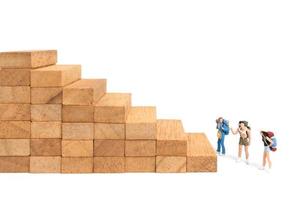 Miniature backpackers standing on wood blocks isolated on a white background, travel concept photo