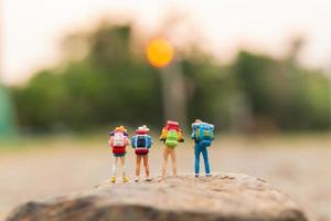Viajeros en miniatura con mochilas caminando sobre una roca, concepto de viaje y aventura