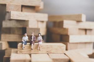 Miniature businesswomen sitting on a wood block with a wooden background photo