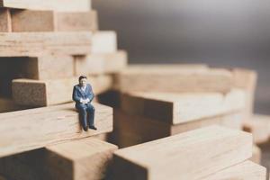 Miniature businessman sitting on a wood block with a wooden background photo