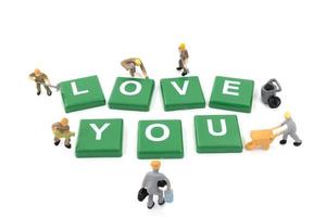 Miniature workers building the word love you on a white background photo