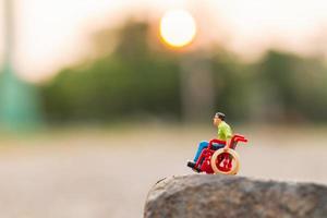 Miniature disabled man sitting in a wheelchair on a rock cliff photo