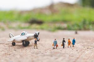 Miniature travelers holding carry-on luggage getting on a plane, exploring the world concept photo