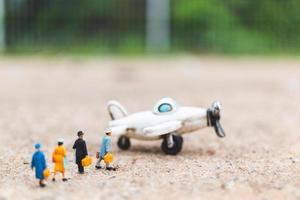 Miniature travelers holding carry-on luggage getting on a plane, exploring the world concept photo