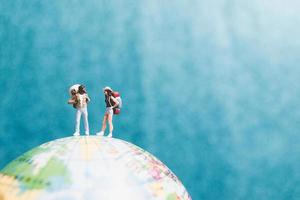 Miniature travelers with backpacks standing on a world globe and walking to a destination photo