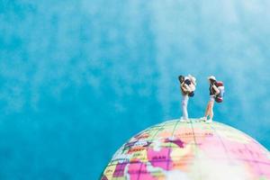 Viajeros en miniatura con mochilas de pie sobre un globo terráqueo y caminando hacia un destino. foto