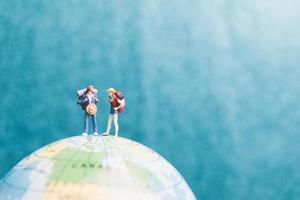 Miniature travelers with backpacks standing on a world globe and walking to a destination photo