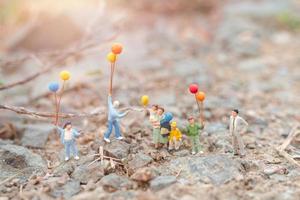 Familia en miniatura caminando en un campo con globos, concepto de tiempo en familia feliz