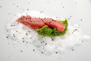 Fresh raw fish fillet steak on ice with pepper and salad on white background photo