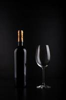 botella de vino y copa con fondo negro foto